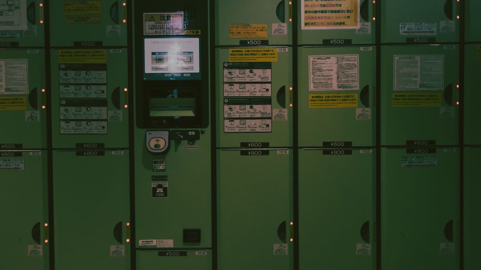 A bank of green coin lockers at a Japanese train station, with fee and instruction stickers on each door