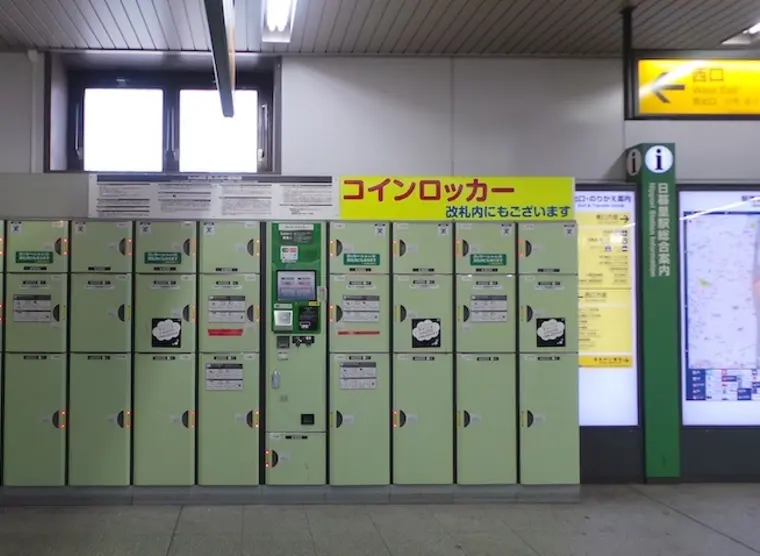 A row of green coin lockers in a Japanese train station under a yellow コインロッカー sign