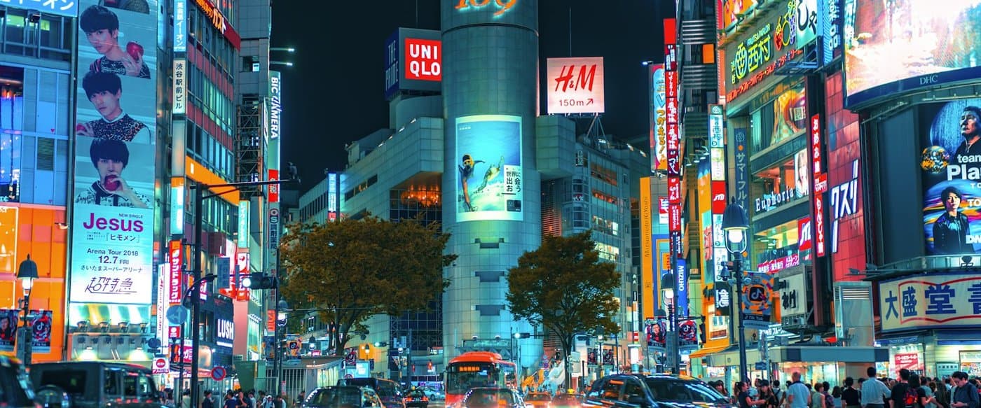 A busy, neon-lit Tokyo street crossing at night